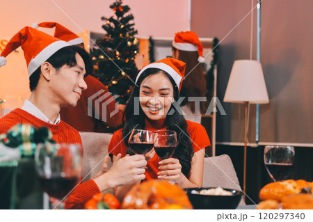 Group of young Asian man and women as friends having fun at a New Year's celebration, holding gift boxes standing by Christmas tree decoration, midnight countdown Party at home with holiday season. 120297340