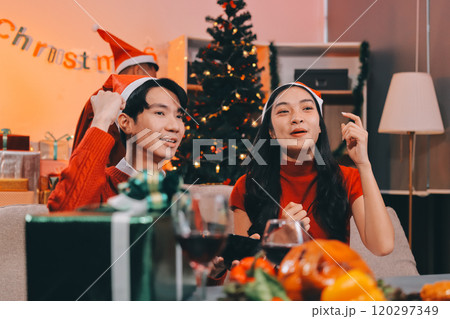 Group of young Asian man and women as friends having fun at a New Year's celebration, holding gift boxes standing by Christmas tree decoration, midnight countdown Party at home with holiday season. 120297349