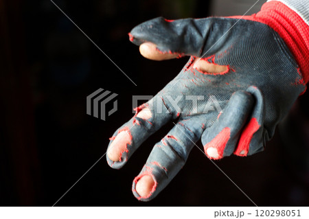 Close-up of a worn-out glove with two damaged fingers against a dark background, symbolizing poverty, hardship, and resilience. Blurred 120298051