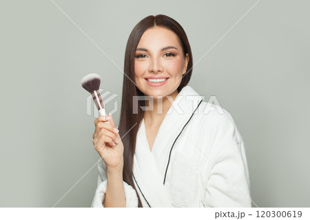Beautiful woman holding makeup brush and smiling, ready to apply cosmetics 120300619