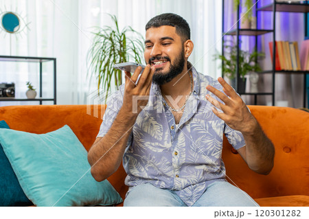 Happy excited Indian man making phone conversation with friends sitting call on couch at home room 120301282