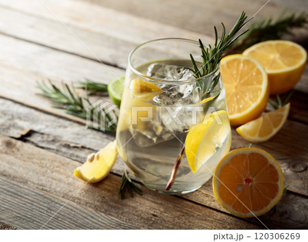 Gin tonic with ice, rosemary, and lemon slices on an old wooden table. Gin tonic with ice, rosemary, and lemon slices on an old wooden table. 120306269