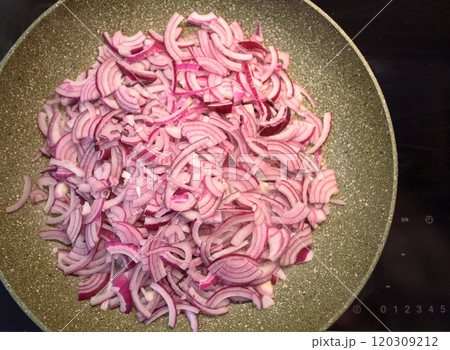 Chopped red onions sizzling in a frying pan on a stovetop during meal preparation Chopped red onions sizzling in a frying pan on a stovetop during meal preparation 120309212