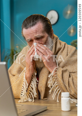 Sick ill senior man suffering from cold flu allergy blows sneezes wipes snot works on laptop at home Sick ill senior man suffering from cold flu allergy blows sneezes wipes snot works on laptop at home 120309549