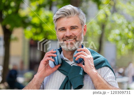 Relaxed smiling mature bearded man listening energetic disco rock n roll music dancing outdoors Relaxed smiling mature bearded man listening energetic disco rock n roll music dancing outdoors 120309731