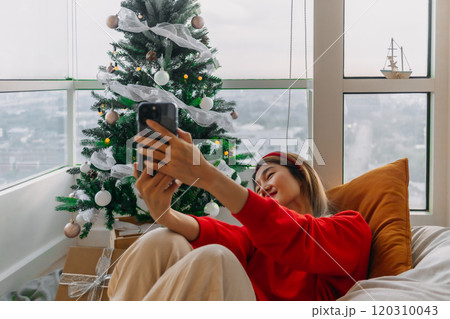 Happy red shirt woman making a video call holiday greeting with her friends and family showing the Christmas tree. Happy red shirt woman making a video call holiday greeting with her friends and family showing the Christmas tree. 120310043