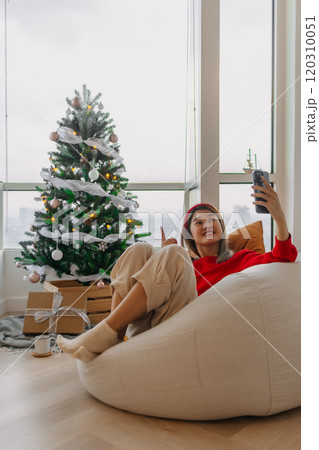 Happy red shirt woman making a video call holiday greeting with her friends and family showing the Christmas tree. Happy red shirt woman making a video call holiday greeting with her friends and family showing the Christmas tree. 120310051