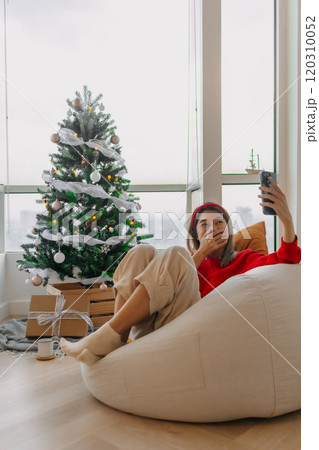 Happy red shirt woman making a video call holiday greeting with her friends and family showing the Christmas tree. Happy red shirt woman making a video call holiday greeting with her friends and family showing the Christmas tree. 120310052