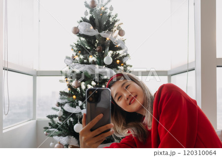 Happy red shirt woman making a video call holiday greeting with her friends and family showing the Christmas tree. Happy red shirt woman making a video call holiday greeting with her friends and family showing the Christmas tree. 120310064