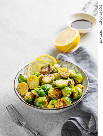 Fried brussels sprouts in a bowl with soy or balsamic sauce, lemon and sesame on a light background with fork and napkin. Fried brussels sprouts in a bowl with soy or balsamic sauce, lemon and sesame on a light background with fork and napkin. 120312153