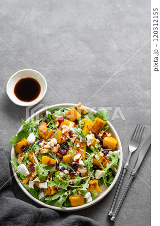 Autumn salad with pumpkin, arugula, feta cheese, nuts and dried berries in plate on dark background Autumn salad with pumpkin, arugula, feta cheese, nuts and dried berries in plate on dark background 120312155