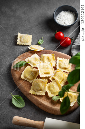 Flat lay of pasta ravioli with tomato and basil on wooden board on dark background with flour Flat lay of pasta ravioli with tomato and basil on wooden board on dark background with flour 120312161