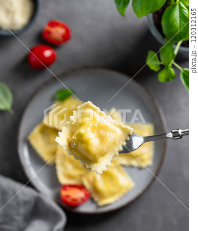 Homemade ravioli pasta with cheese, tomatoes and basil in a plate on a dark background with napkin 120312165