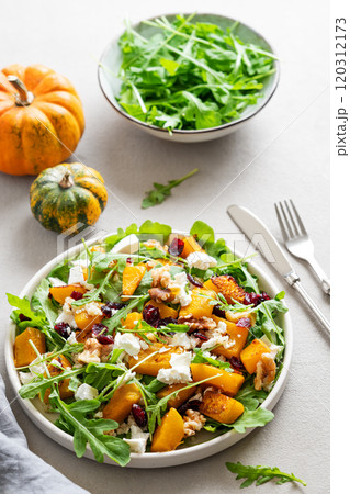 Autumn salad with pumpkin, arugula, feta cheese, nuts and dried berries in a plate  120312173