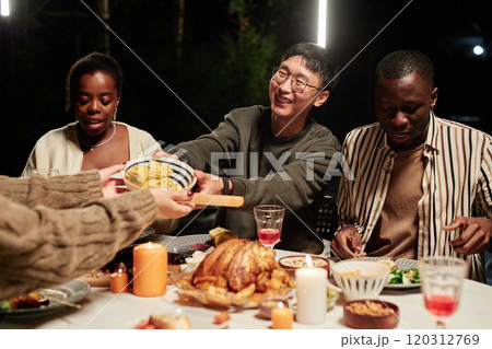 Group of smiling adult friends enjoying meal together outdoors focus on Asian man sharing salad bowl Group of smiling adult friends enjoying meal together outdoors focus on Asian man sharing salad bowl 120312769