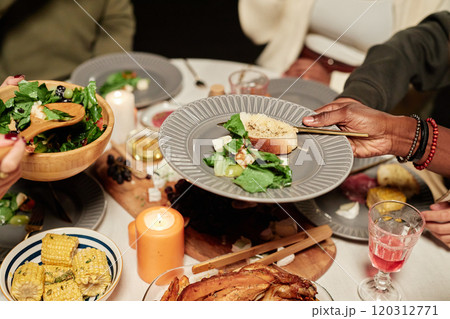 Vibrant close up of festive dinner table with unrecognizable people enjoying meal together and celebrating holidays, focus on hands serving salad 120312771