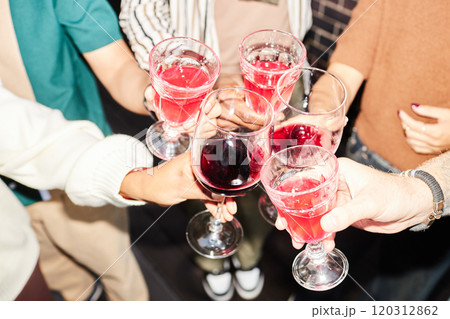 Close up of people holding glasses with red lemonade and cheering while celebrating holidays together at party shot with flash 120312862