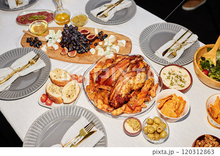At angle shot of golden roasted chicken on dining table served with snacks and dishes for party outdoors shot with flash 120312863