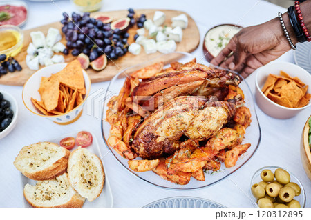 Close up of unrecognizable African American man putting delicious roasted chicken dish with golden potatoes on dining table set for party copy space 120312895