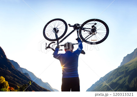 male cyclist with a raised bicycle against the backdrop of the sun and mountains male cyclist with a raised bicycle against the backdrop of the sun and mountains 120313321