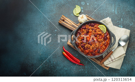 Mexican dish Chili con carne with lime, garlic and chili pepper on dark background top view Mexican dish Chili con carne with lime, garlic and chili pepper on dark background top view 120313654