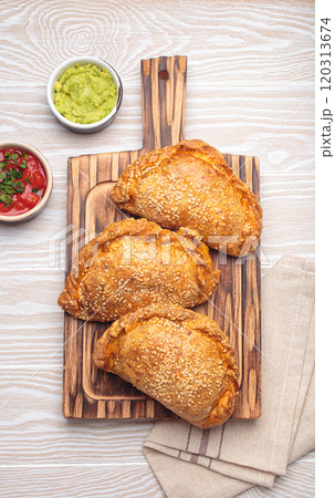 Delicious baked empanadas with sesame seeds served on wooden board with sauces, traditional Spanish savoury pastry 120313674
