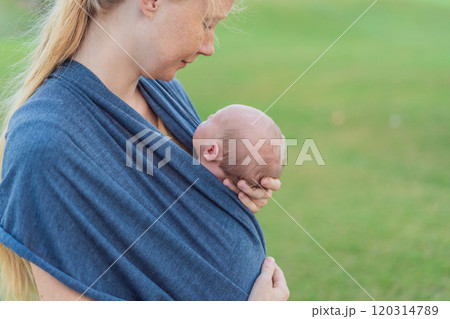 Mom walks with her newborn baby in a sling. This moment highlights the close bond between mother and child, promoting comfort, security, and the benefits of babywearing in everyday life Mom walks with her newborn baby in a sling. This moment highlights the close bond between mother and child, promoting comfort, security, and the benefits of babywearing in everyday life 120314789