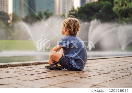 Boy on background of Fountain on the lake in the evening, near by Twin Towers with city on background. Kuala Lumpur, Malaysia Boy on background of Fountain on the lake in the evening, near by Twin Towers with city on background. Kuala Lumpur, Malaysia 120316035