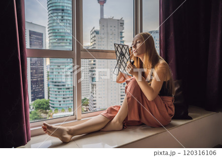 Young woman does makeup sitting by the window with a panoramic view of the skyscrapers and the big city 120316106