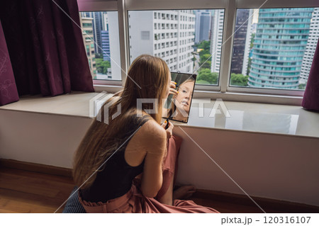 Young woman does makeup sitting by the window with a panoramic view of the skyscrapers and the big city Young woman does makeup sitting by the window with a panoramic view of the skyscrapers and the big city 120316107