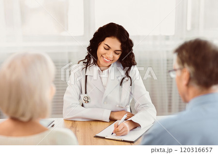 Consultation Concept. Happy latina doctor taking notes about symptoms, filling out medical prescription to senior couple 120316657