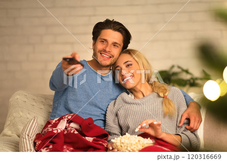 Loving couple watching tv at Christmas eve and eating popcorn at home Loving couple watching tv at Christmas eve and eating popcorn at home 120316669