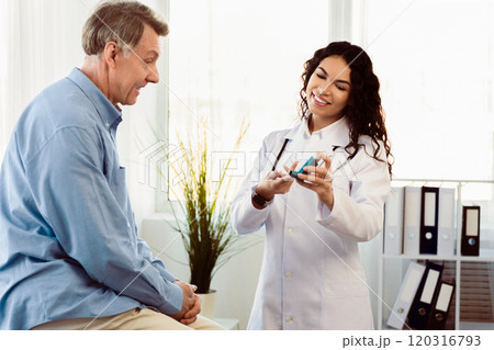 Medicine Concept. Brazilian doctor giving asthma inhaler to elderly man who's sitting on examination table, free space Medicine Concept. Brazilian doctor giving asthma inhaler to elderly man who's sitting on examination table, free space 120316793