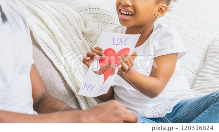 A young girl, smiling brightly, presents her father with a handmade card. The card features a red heart with a brown mustache drawn on it, cropped A young girl, smiling brightly, presents her father with a handmade card. The card features a red heart with a brown mustache drawn on it, cropped 120316824
