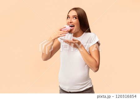 Pregnancy Nutrition. Excited Pregnant Lady Eating Unhealthy Donut Dessert Standing Over White Studio Background. Pregnancy Nutrition. Excited Pregnant Lady Eating Unhealthy Donut Dessert Standing Over White Studio Background. 120316854