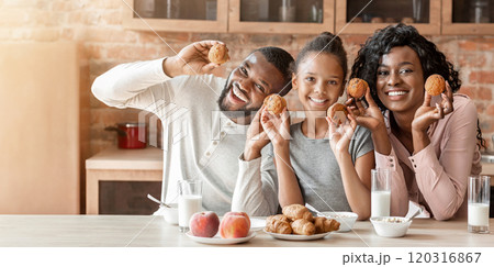 Cheerful african american family having fun during breakfast at kitchen, holding homemade cupcakes 120316867