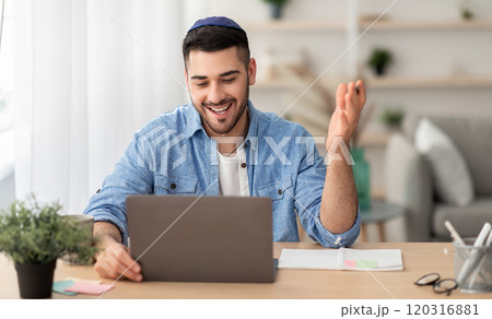 Distant Communication Concept. Portrait of happy jewish male in yarmulke and casual shirt making video call sitting at desk at home office and talking with colleagues, students or family, explaining Distant Communication Concept. Portrait of happy jewish male in yarmulke and casual shirt making video call sitting at desk at home office and talking with colleagues, students or family, explaining 120316881