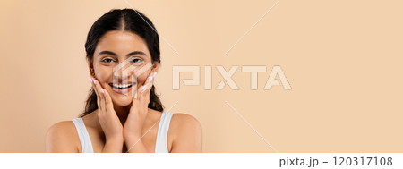 Skincare Concept. Beautiful smiling young indian woman touching face and looking at camera, attractive eastern lady enjoying her flawless skin, standing over beige studio background, copy space Skincare Concept. Beautiful smiling young indian woman touching face and looking at camera, attractive eastern lady enjoying her flawless skin, standing over beige studio background, copy space 120317108