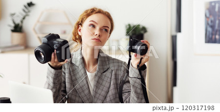 A woman in a gray blazer holds two digital cameras, considering which one to choose. A woman in a gray blazer holds two digital cameras, considering which one to choose. 120317198