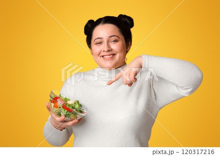 Weight-loss Plan Concept. Happy Plus Sized Woman Pointing At Bowl With Fresh Vegetable Salad In Her Hands, Yellow Background, Empty Space 120317216