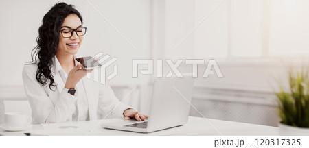 Voice Search. Mexican businesswoman using smart phone voice recognition to send message at workplace. Empty space Voice Search. Mexican businesswoman using smart phone voice recognition to send message at workplace. Empty space 120317325