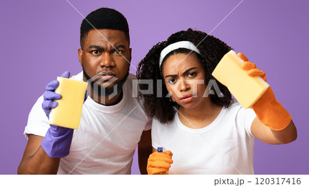 Household Chores. Serious black couple holding sponges and sprayer, ready to clean dust from camera, standing over pink background with copy space Household Chores. Serious black couple holding sponges and sprayer, ready to clean dust from camera, standing over pink background with copy space 120317416