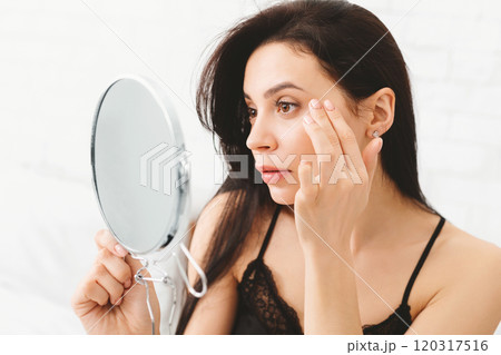 A woman is standing in front of a mirror, closely inspecting her reflection. She appears focused and thoughtful as she examines her features. 120317516