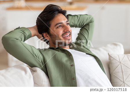 Arab man with a beard is sitting on a white couch with his arms behind his head, looking relaxed and content. The background appears to be a living room. Arab man with a beard is sitting on a white couch with his arms behind his head, looking relaxed and content. The background appears to be a living room. 120317518