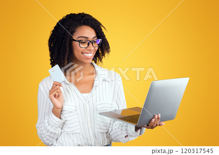 Online Banking. Afro girl in eyewear holding credit card and laptop over yellow background Online Banking. Afro girl in eyewear holding credit card and laptop over yellow background 120317545