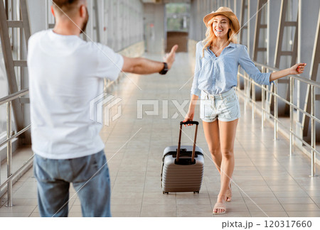 Meet And Greet Concept. Back view portrait of man greeting woman with open arms at the airport terminal Meet And Greet Concept. Back view portrait of man greeting woman with open arms at the airport terminal 120317660
