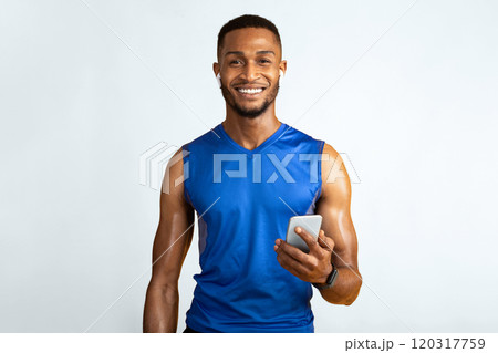 Working Out. Smiling afro man in earbuds holding smartphone, using fitness app isolated on yellow studio wall, copyspace Working Out. Smiling afro man in earbuds holding smartphone, using fitness app isolated on yellow studio wall, copyspace 120317759