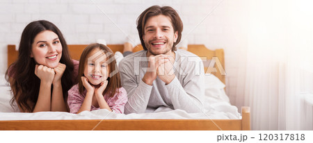 Portrait of happy family of three with little daughter posing on bed at home together and smiling to camera, free space Portrait of happy family of three with little daughter posing on bed at home together and smiling to camera, free space 120317818