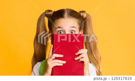Back To School Anxiety. Scared Elementary Student Girl Hiding Behind Book On Yellow Studio Background. Free Space 120317819
