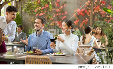 Waiter takes an order from a couple in love who decided to meet in an open air restaurant 120321401